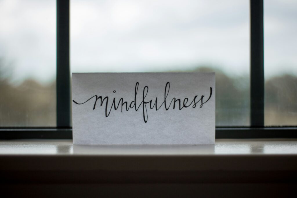 Schriftzug 'Mindfulness' in eleganter Handschrift auf einem Blatt Papier vor einem Fenster, das auf Achtsamkeit hinweist.