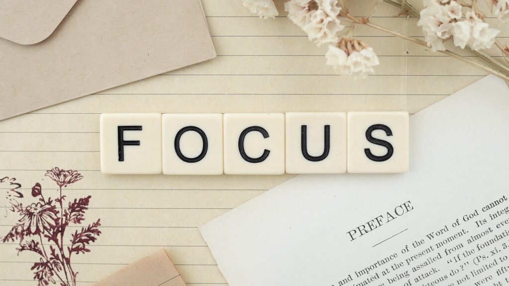 Scrabble-Buchstaben, die das Wort 'FOCUS' bilden, auf einem Notizblatt mit Blumenverzierung im Hintergrund.