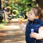 Kleines Mädchen spielt im Freien und pustet Seifenblasen – Symbol für kindliche Unbeschwertheit.