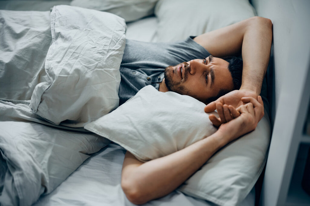 Mann liegt wach im Bett, die Hände am Kopf