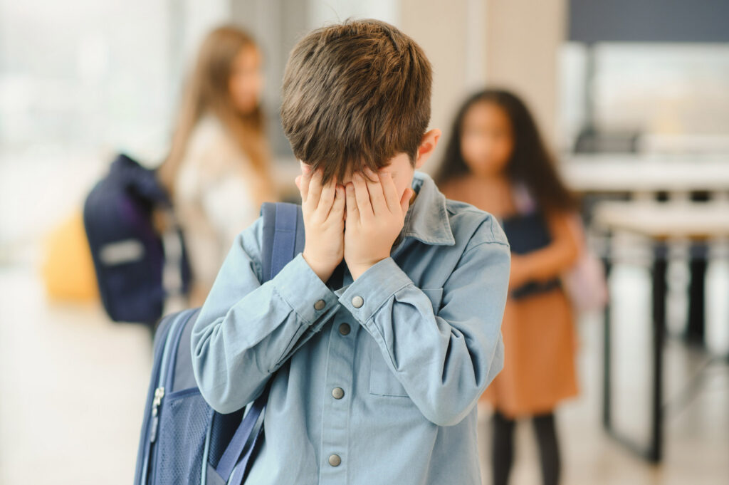 Junge hält sich im Schulflur die Hände vors Gesicht