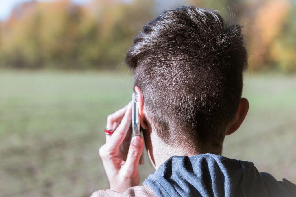 Rückansicht eines Jungen, der mit dem Smartphone telefoniert.