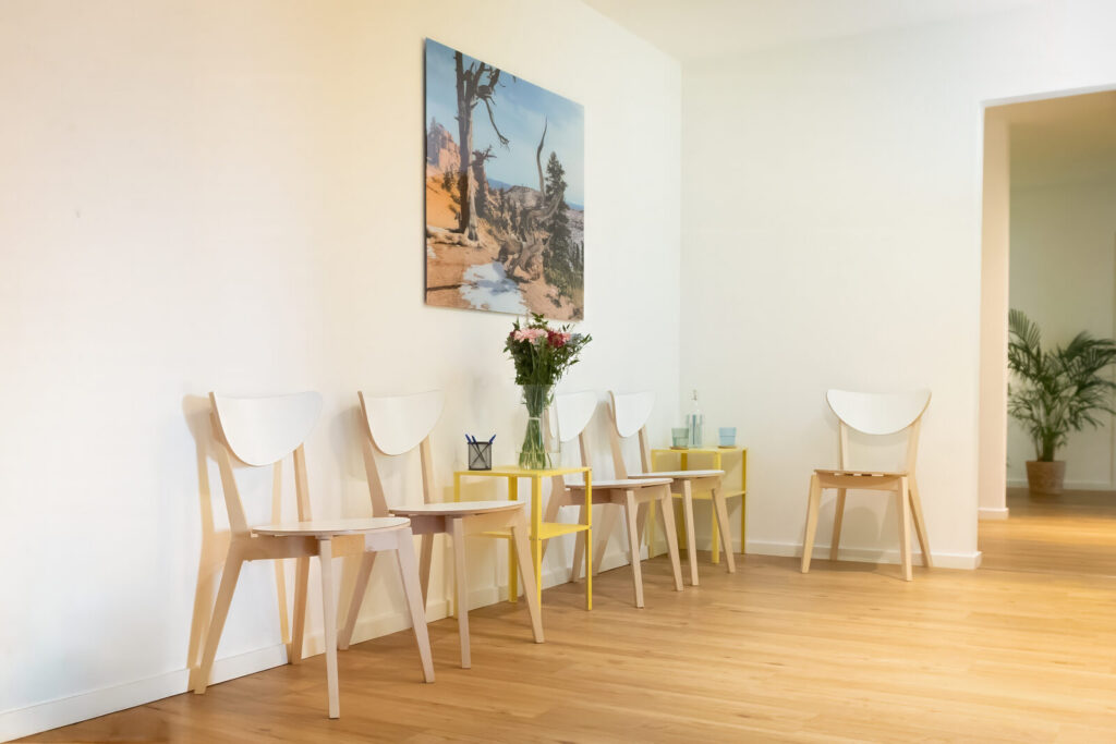 Wartebereich mit Holzstühlen, gelben Beistelltischen und Blumen