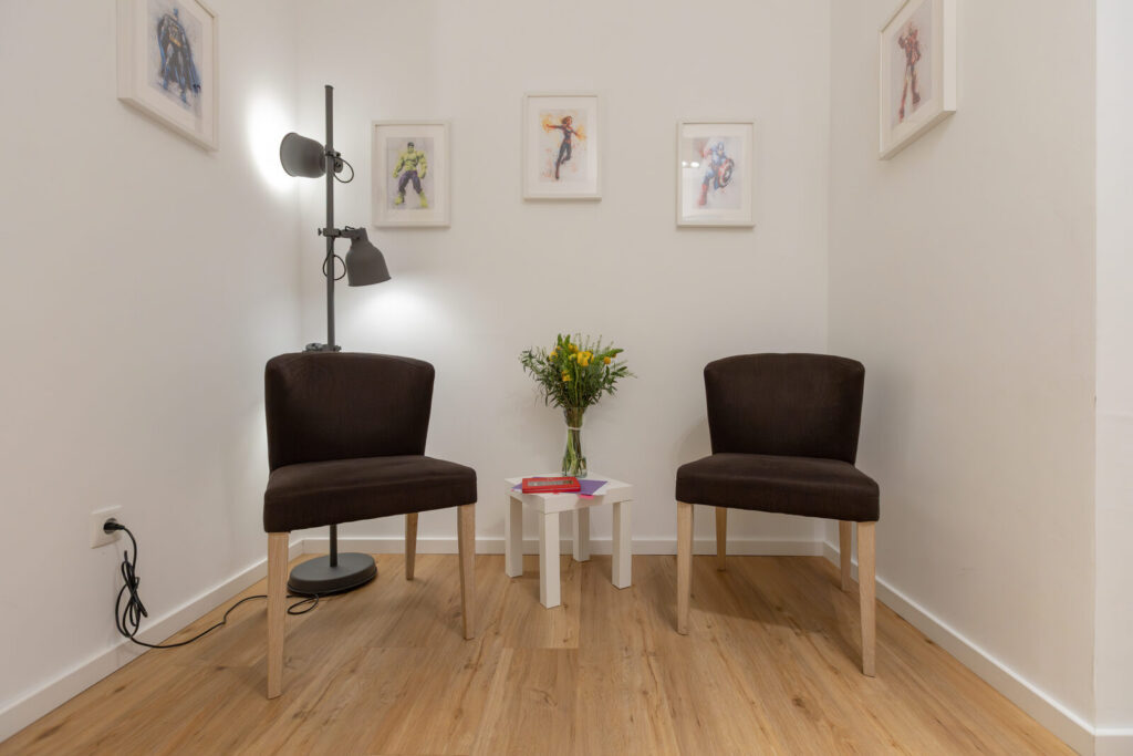 Behandlungsraum mit zwei Stühlen, Stehlampe und Superhelden-Bildern an der Wand